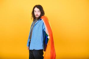 gut aussehend jung Mann mit Stolz Bewegung lgbt Regenbogen Flagge auf Schulter gegen Weiß Hintergrund. Mann mit ein Fröhlich Stolz Flagge. foto