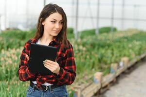 schön jung lächelnd Mädchen, Arbeiter mit Blumen im Gewächshaus. Konzept Arbeit im das Gewächshaus, Blumen. foto