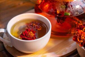 Ringelblume Blume gesund Tee im Glas Becher mit Tee Topf auf Garten Tisch. Kräuter- Medizin köstlich Tisane Tee mit frisch Gelb blühen Löwenzahn Blumen Tee Tasse. Grün Clearing Infusion Wildblumen Öko freundlich nachhaltig Essen foto