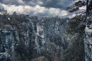 robust Felsen beim Basteibridge während Schneefall. breit Aussicht Über Bäume und Berge foto