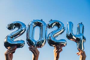 glücklich Neu Jahr 2024 metallisch Luftballons auf Blau Himmel Hintergrund. Gruß Karte Silber vereiteln Luftballons Zahlen Weihnachten Urlaub Konzept. Feier Party Glückwunsch Dekoration foto