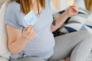 schwanger Frau im Bett im das Schlafzimmer halten ein Frage Karte, Junge oder Mädchen. foto