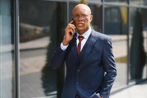 Porträt von ein jung afrikanisch amerikanisch Geschäftsmann reden auf Zelle Telefon während draußen im das Stadt foto