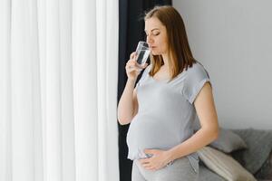 Porträt von ein schön schwanger Frau Trinken Wasser foto