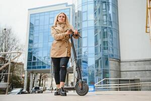 jung Frau auf Elektro Roller im Stadt. Frau Reiten Roller im Sonnenuntergang Licht im Straße foto