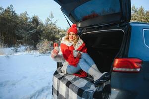 jung Frau Sitzung im Auto Kofferraum Trinken warm Tee und nimmt ein Selfie beim Winter geschneit Tag. foto