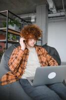 kaukasisch Hipster Kerl genießen Entfernung Job im Kaffee Geschäft, männlich Freiberufler im modisch Brille Sitzung im Cafeteria mit modern Laptop Gerät foto