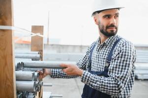 ein Arbeiter hält Metall Rohre im ein Fabrik Lagerhaus. Metall rollen foto