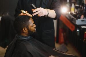Nahansicht von Prozess von Trimmen von Haar im Barbier Geschäft. qualifiziert Barbier behalten Clipper im Hände und korrigieren gestalten von Haar zu männlich Klient Sitzung auf Stuhl. Konzept von Haarschnitt und Rasieren. foto