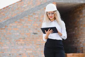 absorbiert im das Arbeit von ein Frau Ingenieur Arbeiten mit ein Tablette auf das Hintergrund von das Konstruktion Seite? ˅. Porträt von ein jung Architekt, schützend Ausrüstung. selektiv Fokus foto