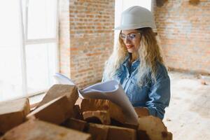 Konstruktion Konzept. ziemlich weiblich Baumeister im Overall und Helm Arbeiten auf Konstruktion Seite? ˅. foto