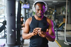 sportlich Mann Stehen im ein Fitnessstudio Hören zu Musik- mit kabellos Kopfhörer foto