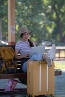 Mädchen mit ein Laptop während warten im ein Zug Bahnhof, Mädchen auf Zug Bahnhof mit Gepäck Arbeiten auf Laptop Computer, Laptop im verwenden, sitzt mit ein Koffer foto