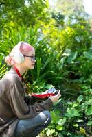 schön jung Künstler Frau nehmen Foto im Blumen Garten. jung süß Mädchen tragen das Kamera im das Garten