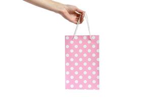 Hand halten Rosa Polka Punkt Tasche auf Weiß Hintergrund. Präsentation von das Geschenk. Kauf im Verpackung foto