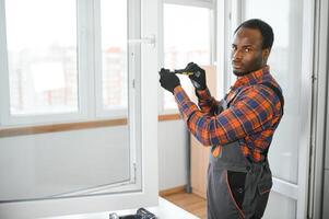 ein afrikanisch Handwerker Instandsetzung, passt sich an oder installiert Metall-Kunststoff Fenster im das Wohnung foto