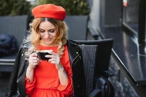 jung stilvoll Frau im rot Baskenmütze haben ein Französisch Frühstück mit Kaffee und Croissant Sitzung oudoors beim das Cafe Terrasse foto