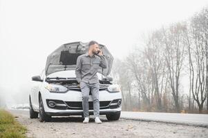 traurig Mann auf das Straße Nächster zu das gebrochen Auto foto