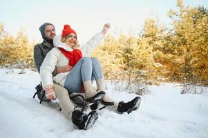ein Seite Aussicht von ein glücklich Paar haben Spaß während gleiten bergab zusammen Über schneebedeckt Steigung mit ein Schlitten foto