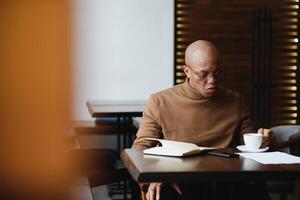 Planung das Tag. Ruhe schwarz Schüler Schreiben seine Lektion Zeitplan im Notizbuch, Sitzung im modern Bar, leeren Raum. foto