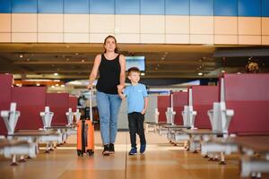 Familie beim Flughafen Vor Flug. Mutter und Sohn warten zu Tafel beim Abfahrt Tor von modern International Terminal. Reisen und fliegend mit Kinder. Mama mit Kind Einsteigen Flugzeug. Gelb Familie foto