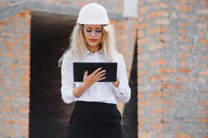 absorbiert im das Arbeit von ein Frau Ingenieur Arbeiten mit ein Tablette auf das Hintergrund von das Konstruktion Seite? ˅. Porträt von ein jung Architekt, schützend Ausrüstung. selektiv Fokus foto