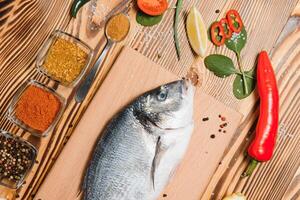 frisch roh Dorado Fisch auf Backen Papier mit Zitrone, Pfeffer, Tomaten und verschiedene Gewürze auf hölzern Hintergrund mit Kopieren Raum. foto