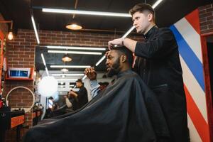 afrikanisch männlich Klient bekommen Haarschnitt beim Barbier Geschäft von Fachmann Friseur. foto
