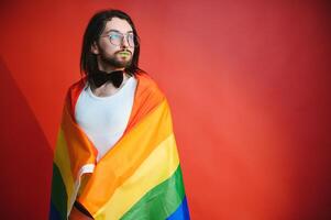 gut aussehend jung Mann mit Stolz Bewegung lgbt Regenbogen Flagge auf Schulter gegen Weiß Hintergrund. Mann mit ein Fröhlich Stolz Flagge. foto