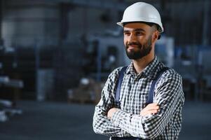 glücklich Fachmann schwer Industrie Ingenieur Arbeiter tragen Uniform, und schwer Hut im ein Stahl Fabrik. lächelnd industriell Spezialist Stehen im ein Metall Konstruktion Herstellung foto