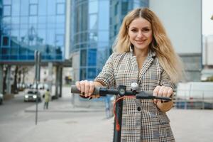 jung Frau auf Elektro Roller im Stadt. Frau Reiten Roller im Sonnenuntergang Licht im Straße foto