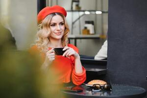 jung stilvoll Frau im rot Baskenmütze haben ein Französisch Frühstück mit Kaffee und Croissant Sitzung oudoors beim das Cafe Terrasse foto