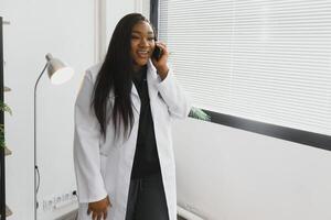 lächelnd weiblich Arzt mit Handy, Mobiltelefon Telefon im das Krankenhaus. foto