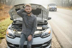 traurig Treiber halten seine Kopf haben Motor Problem Stehen in der Nähe von gebrochen Auto auf das Straße. Auto Nervenzusammenbruch Konzept foto