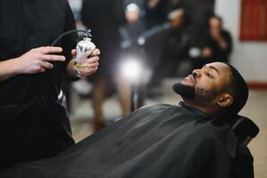 afrikanisch männlich Klient bekommen Haarschnitt beim Barbier Geschäft von Fachmann Friseur. foto