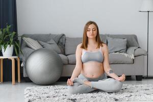 Nahansicht Schuss von unkenntlich schwanger Frau meditieren beim heim, erwartungsvoll Dame Sitzung im Lotus Position mit umklammert Hände, üben Yoga zum gesund Schwangerschaft, abgeschnitten Bild mit kostenlos Raum foto