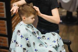 Seite Aussicht von süß wenig Junge bekommen Haarschnitt durch Friseur beim das Friseurladen. foto