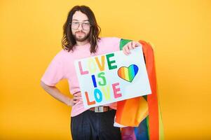 gut aussehend jung Mann mit Stolz Bewegung lgbt Regenbogen Flagge auf Schulter gegen Weiß Hintergrund. Mann mit ein Fröhlich Stolz Flagge. foto