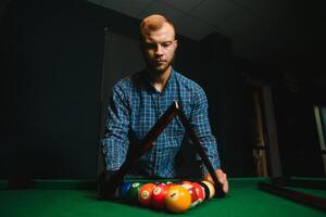 junger Mann, der Billard im dunklen Billardklub spielt foto