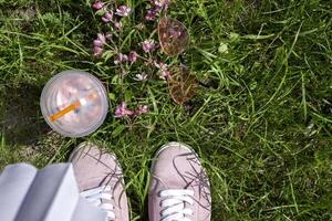 Rosa Gläser, Blühen Ast und frisch trinken in der Nähe von Rosa Turnschuhe gegen ein Grün Gras Hintergrund. foto