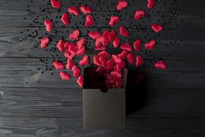 rot Herzen sind gegossen aus von ein schwarz Geschenk Box auf ein dunkel Blau hölzern Tisch. foto