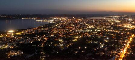 ein Panorama- Antenne Aussicht von das Stadt in der Nähe von Meer beim Nacht. foto