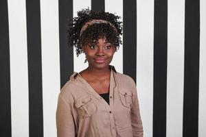 zur Seite schauen. Lächelndes afroamerikanisches Mädchen steht im Studio mit vertikalen weißen und schwarzen Linien im Hintergrund