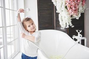 lustiges kleines Mädchen mit lockigem Haar. machen Sie sich bereit, ein Bad zu nehmen. geräumiges beleuchtetes Badezimmer. das Konzept eines gesunden und sauberen Körpers. seit der Kindheit für sich selbst sorgen foto