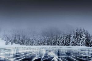 majestätische Winterlandschaft mit Rissen auf der Oberfläche des blauen Eises. zugefrorener See in den Winterbergen. eine dramatische Szene mit niedrigen schwarzen Wolken, eine Ruhe vor dem Sturm foto