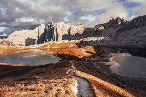 der Weg zwischen zwei kleinen Seen, der zu den großen Dolomiten führt, die im Sonnenlicht stehen foto