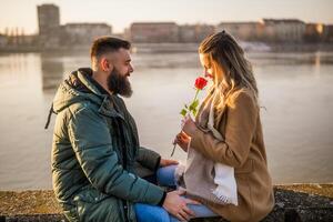 Mann geben rot Rose zu seine Frau während Sie genießen Ausgaben Zeit zusammen draussen. foto