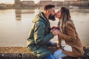 glücklich Paar küssen während Mann geben die Geschenke zu seine Frau draussen. foto