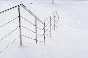 Metall Treppe mit Geländer auf das Straße. das Schritte und Geländer von das Treppe sind bedeckt mit Schnee. sanft absteigen und aufsteigen foto