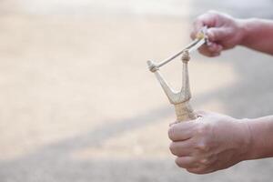 schließen oben Hände halt hölzern Schleuder zum spielen Schießen Spiel. Konzept , thailändisch traditionell Waffe Das verwenden zu schießen Vögel, Fisch , zum Kampf Spiel oder andere Zwecke. foto